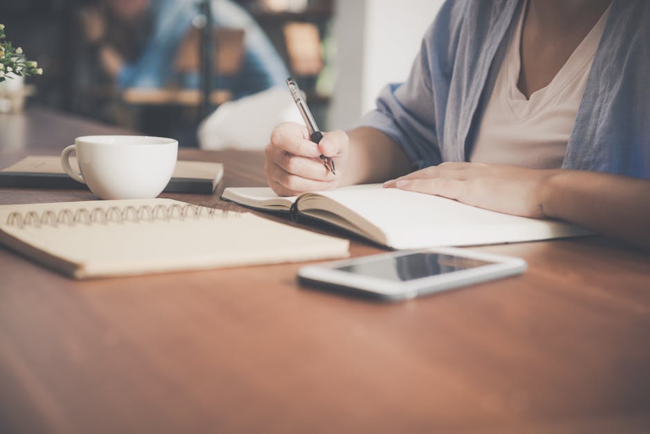 Person writing notes in a notebook with a smartphone nearby.