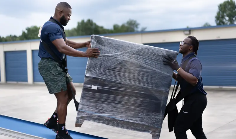 Two men loading a large wrapped item onto a truck.